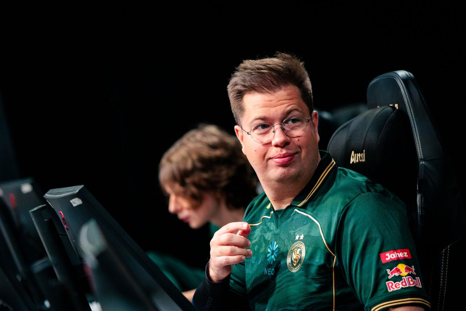 karrigan with a slight smile at his desk, kyousuke is in the background